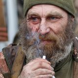 Ein älterer weißer Mann mit grau-weiße Vollbart trägt Uniform und raucht eine Zigarette. Um sein rechtes Auge sind Wunden