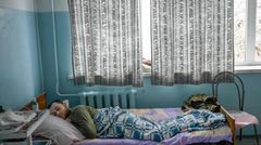In einem metallenen Krankenhausbett liegt ein junger weißer Mann auf dem Bauch und schläft