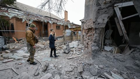 Eine Frau und ein Soldat stehen vor einem zerstörten Gebäude bei Donezk