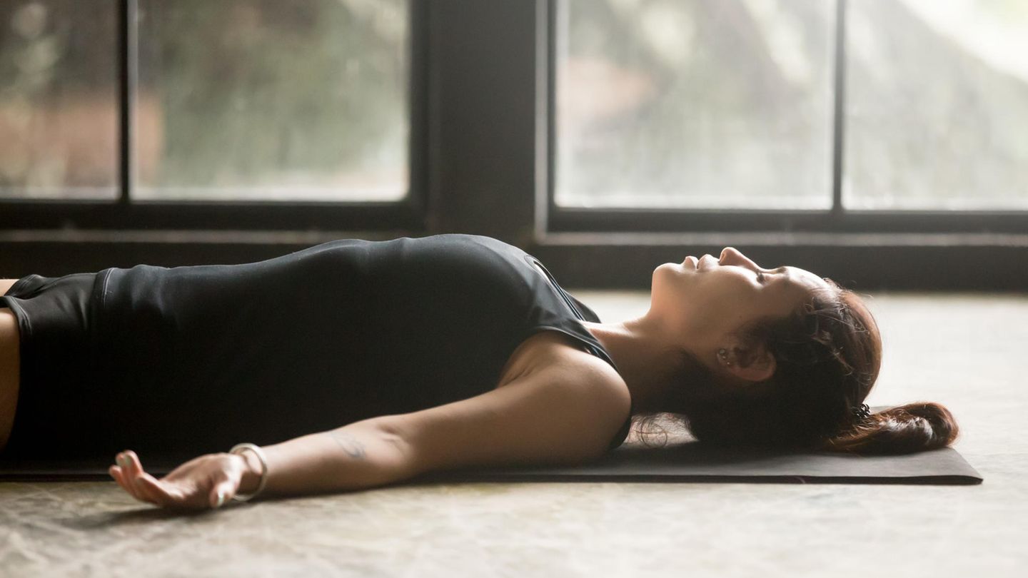 Frau liegt während dem Yoga auf dem Boden