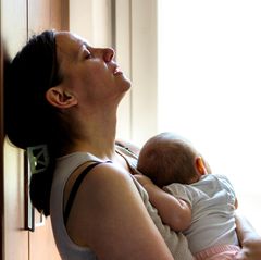Regretting Motherhood: Eine Mutter lehnt verzweifelt an einem Schrank, mit ihrem Baby im Arm