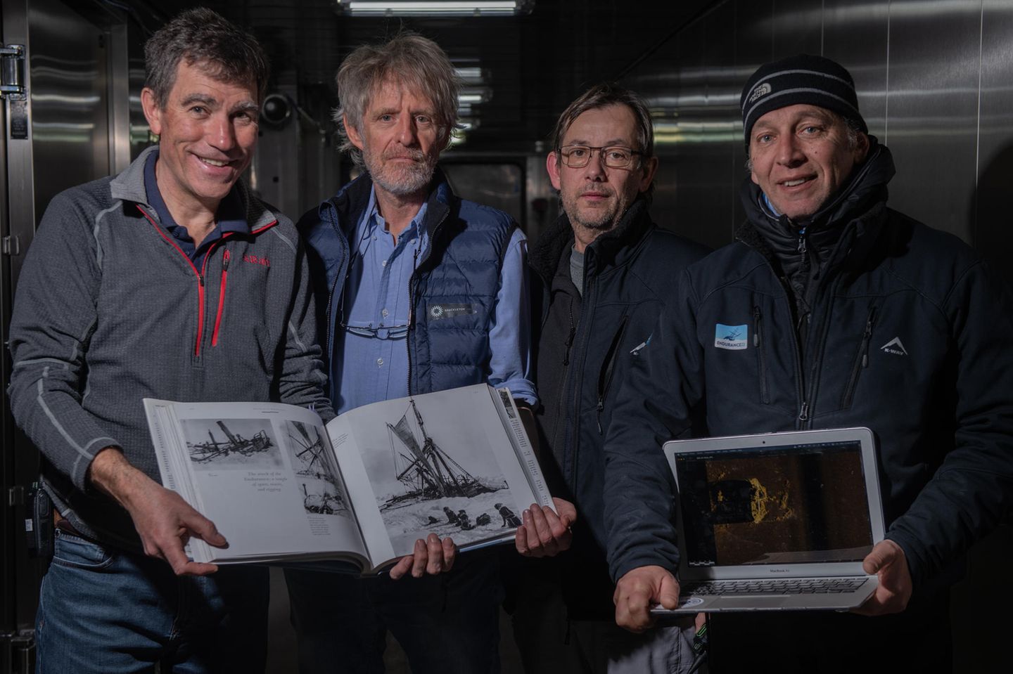 Vier Männer zeigen ein Buch und den Scan des Unterwasserroboters