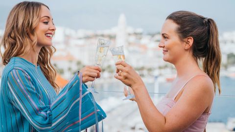 Zwei Frauen stoßen auf einer Dachterrasse mit Champagner an