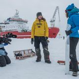 Drei Personen stehen neben dem Schiff auf dem Eis