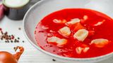 Veganer Borschtsch mit Knödeln  Zutaten für 6 Personen:   1⁄4 Selleriewurzel, 1 Karotte, 3-4 Kartoffeln, 1 Rote Bete, 2 Lorbeerblätter, 3 Pimentbeeren, 2-3 Knoblauchzehen,  1⁄2 Weißkohl, 3-4 EL Pflanzenöl, 1⁄2 rote Paprika, 1 Zwiebel, 1 Tasse Tomatensaft, Salz, Pfeffer  Der Teig für Knödel: 150 g Mehl Typ 405, 75 g Wasser, 1 EL Pflanzenöl  Zubereitung:  1. Für die Nockerl: Mehl mit Wasser, einer Prise Salz und 1 EL Öl zu einem elastischenTeig kneten. Der Teig solltel nicht mehr kleben. Unter einem Handtuch oder unter Frischhaltefolie 20 Minuten im Kühlschrank ruhen lassen.  2. Dann die Gemüsebrühe kochen: Dafür Sellerie und Karotten in große Würfel, Kartoffeln und Rote Bete in kleine Würfel schneiden und in einen großen Topf geben. Mit zwei Liter Wasser aufgießen. Mit Lorbeerblättern, Pimentbeeren und kleingeschnittenen Knoblauch würzen.  3. Kohl fein schneiden und zum kochenden Borschtsch geben.  4. Öl in einer Pfanne erhitzen und kleingeschnittene Paprika sowie Zwiebel braten, dann den Tomatensaft hinzufügen. So lange einkochen lassen, bis eine Breikonsistenz entsteht. Zum Borschtsch geben.  5. Den Teig in kleine Teigstücke zupfen und zu Knödeln formen. In den kochenden Borschtsch geben. Wenn die Knödel an der Oberfläche schwimmen, sind sie gar. Nach Bedarf salzen und pfeffern. 