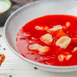 Veganer Borschtsch mit Knödeln  Zutaten für 6 Personen:   1⁄4 Selleriewurzel, 1 Karotte, 3-4 Kartoffeln, 1 Rote Bete, 2 Lorbeerblätter, 3 Pimentbeeren, 2-3 Knoblauchzehen,  1⁄2 Weißkohl, 3-4 EL Pflanzenöl, 1⁄2 rote Paprika, 1 Zwiebel, 1 Tasse Tomatensaft, Salz, Pfeffer  Der Teig für Knödel: 150 g Mehl Typ 405, 75 g Wasser, 1 EL Pflanzenöl  Zubereitung:  1. Für die Nockerl: Mehl mit Wasser, einer Prise Salz und 1 EL Öl zu einem elastischenTeig kneten. Der Teig solltel nicht mehr kleben. Unter einem Handtuch oder unter Frischhaltefolie 20 Minuten im Kühlschrank ruhen lassen.  2. Dann die Gemüsebrühe kochen: Dafür Sellerie und Karotten in große Würfel, Kartoffeln und Rote Bete in kleine Würfel schneiden und in einen großen Topf geben. Mit zwei Liter Wasser aufgießen. Mit Lorbeerblättern, Pimentbeeren und kleingeschnittenen Knoblauch würzen.  3. Kohl fein schneiden und zum kochenden Borschtsch geben.  4. Öl in einer Pfanne erhitzen und kleingeschnittene Paprika sowie Zwiebel braten, dann den Tomatensaft hinzufügen. So lange einkochen lassen, bis eine Breikonsistenz entsteht. Zum Borschtsch geben.  5. Den Teig in kleine Teigstücke zupfen und zu Knödeln formen. In den kochenden Borschtsch geben. Wenn die Knödel an der Oberfläche schwimmen, sind sie gar. Nach Bedarf salzen und pfeffern. 