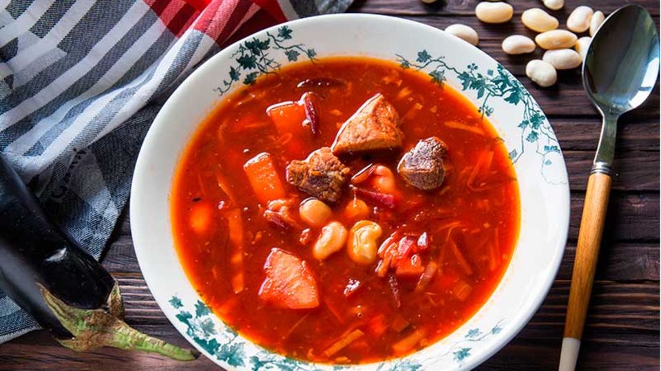 Traditioneller Borschtsch  Zutaten:  300 g fleischige Schweinerippchen, 1 mittelgroße Rote Bete, 1 große Karotte, 2 mittelgroße Kartoffeln, 100 g getrocknete Bohnen, 150 g Aubergine, 150 g Kohl, 2 EL Tomatenmark, 1 EL Kristallzucker, 2 Lorbeerblätter, 2 Knoblauchzehen, 2 EL Pflanzenöl (am besten Sonnenblumenöl), Schwarze Pfefferkörner, Salz, und gemahlener Pfeffer  Zubereitung:  1. Die Rote Bete waschen und anderthalb Stunden im Ofen backen (oder bis sie weich sind), abkühlen lassen, schälen und in Julienne schneiden oder mit einer Reibe zerkleinern. Klappt auch mit vorgekochter Roter Bete aus dem Supermarkt.  2. Die getrockneten Bohnen im kalten Wasser für eine Stunde einweichen. Danach aus dem Wasser nehmen.  3. Das Fleisch leicht salzen und zusammen mit dem Knoblauch, dem Lorbeerblatt und einigen Pfefferkörnern in eine ofenfeste Form geben. 20 Minuten bei 180 °C backen. Das Backen des Fleisches vor der Zubereitung der Brühe intensiviert den Geschmack der Suppe. Das Fleisch abkühlen lassen und in Stücke schneiden.  4. Die Karotte grob reiben, die Zwiebel und die Aubergine fein würfeln. Etwas Öl in einer Bratpfanne erhitzen und Karotte und Zwiebel etwa 2-3 Minuten anbraten. Fügen Sie die Aubergine und die Rote Bete hinzu und braten Sie alles für weitere 2 Minuten. Tomatenmark und Zucker dazugeben und weitere zwei Minuten garen.  5. Kartoffenl schälen und in mittelgroße Würfel schneiden. Die Kartoffeln in einen großen Topf geben und mit zwei Liter Wasser auffüllen. Dann das Fleisch dazugeben und für weitere fünf Minuten köcheln lassen.  6. Den fein geraspelten Kohl und die Bohnen dazugeben und für ca. 15 Minuten weiterkochen. Dann das restliche Gemüse dazugeben und für fünf Minuten garen. Salz und Pfeffer nach Geschmack. Ganz zum Schluss etwas zerdrückten Knoblauch dazugeben und vom Herd nehmen.