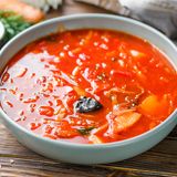 Ukrainischer Borschtsch mit Schweinerippchen  Zutaten:   400-500 g Schweinerippchen, 2 Rote Bete, 2 Tomaten, ¼ Selleriewurzel, ¼ Kohlkopf, 3-4 Kartoffeln, 1-2 Karotten, 1 Zwiebel, 2 Lorbeerblätter, 3 Gewürznelken, Piment, 1 Knoblauchzehe, 1 rote Paprika, 200 ml Tomatensaft, 30 g ungesalzene Butter, 2 EL Tomatenmark, Salz  Außerdem: Saure Sahne und gehackter Dill zum Abschmecken  Zubereitung:  1. Backofen auf 200°C vorheizen. Die Schweinerippchen in einer ofenfesten Form etwa 30 Minuten backen bis sich eine goldene Kruste bildet. In der Zwischenzeit die Selleriewurzel waschen und grob hacken. Es ist nicht nötig, sie zu schälen. Schneiden Sie die Karotten in Stücke von etwa der gleichen Größe wie die Selleriestücke. Die gebackenen Rippchen in einen großen Topf geben, etwa 3 Liter Wasser hinzufügen. Fügen Sie die Sellerie- und Karottenstücke und eine halbe ungeschälte Zwiebel hinzu. Zum Kochen bringen und bei mittlerer Hitze etwa 30 Minuten köcheln lassen.  2. Jetzt das Gemüse: Das macht jeden Borschtsch so aromatisch. Die rote Paprika würfeln. Die Tomaten und die andere Hälfte der Zwiebel fein würfeln. Die Butter in einer Pfanne erhitzen und das Gemüse dünsten, bis es weich wird. 200ml Tomatensaft und ca. 2 EL Tomatenmark dazugeben und weitere 5-7 Minuten garen. Die eine Rote Bete grob reiben und zum Gemüse hinzugeben. Weitere 3-4 Minuten kochen lassen. Die andere Rote Bete entsaften oder sehr fein reiben.  3. Das ganze Gemüse mit Piment und Lorbeerblättern in den Topf mit den Rippchen geben. Nach Geschmack salzen.  4. Kartoffeln waschen und schälen, grob Würfeln und in den Topf geben. Knoblauchzehen halbieren und auch dazugeben.  5. Den Kohl in Streifen schneiden und beiseite stellen, erst ganz zum Schluss wird er in den Borschtsch gegeben.  6. Sobald alle Zutaten weich sind, den zerkleinerten Kohl in den Topf geben. 5 weitere Minuten garen und den Borschtsch vom Herd nehmen. Lassen Sie die Suppe mindestens eine halbe Stunde ruhen, bevor Sie sie mit saurer Sahne und fein gehacktem Dill servieren. Bewahren Sie den Borschtsch im Kühlschrank auf und denken Sie daran, dass er über Nacht noch köstlicher wird.