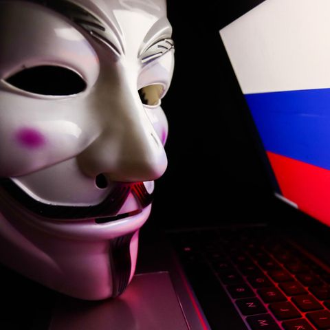 Die für Anonymous typische Maske liegt auf einem Laptop, der die russische Flagge zeigt