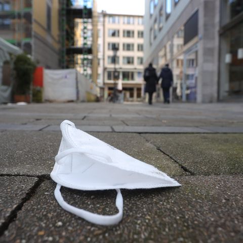 In einer Fußgängerzone in München liegt eine FFP2-Maske am Boden. Im Hintergrund gehe unscharf zwei Passanten weg