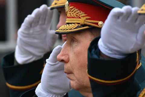 Ein älterer weißer Mann steht in Gardeuniform mit schwarz-rot-goldener Mütze und weißem Handschuh salutierend in Reih und Glied