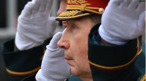Ein älterer weißer Mann steht in Gardeuniform mit schwarz-rot-goldener Mütze und weißem Handschuh salutierend in Reih und Glied