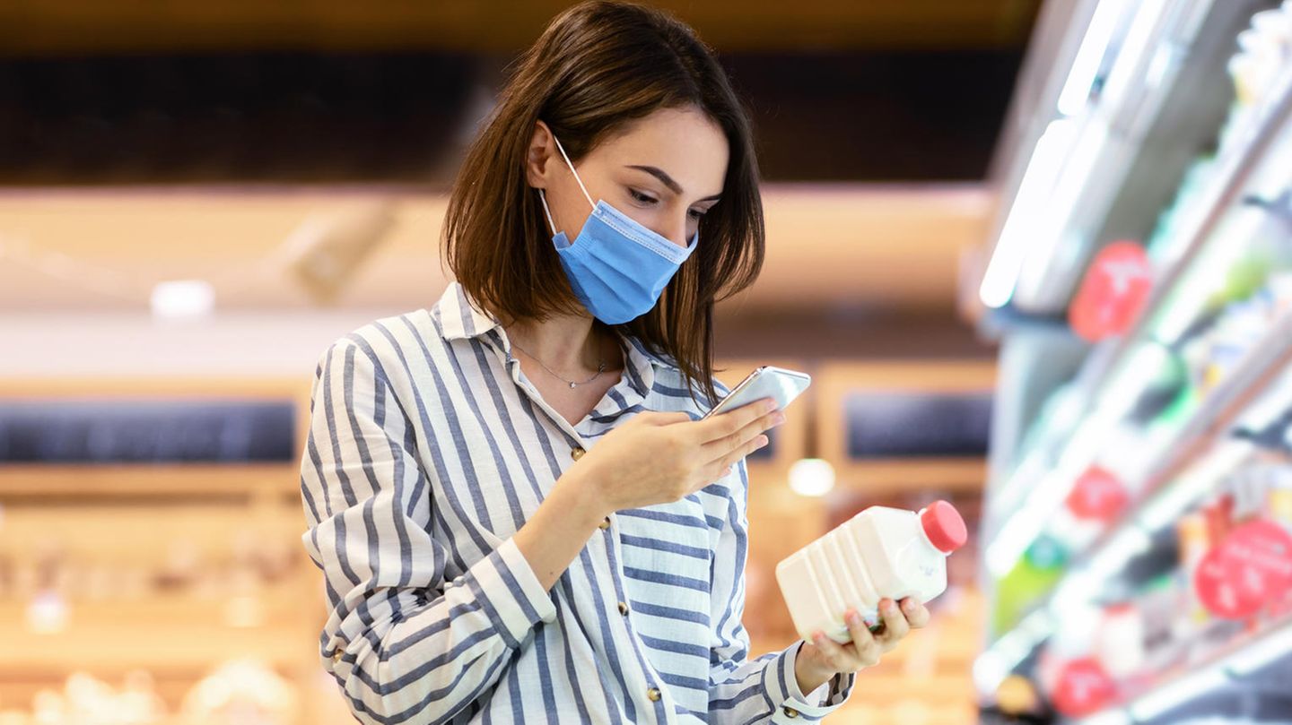 Eine Frau schaut mit Maske in ihr Smartphone