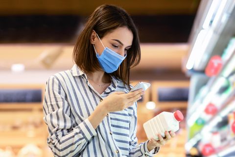 Eine Frau schaut mit Maske in ihr Smartphone