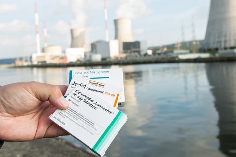 Hand hält mehrere Packungen Jodtabletten vor einem Atomkraftwerk