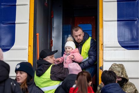 Zwei Männer heben ein Kleinkind am Bahnhof von Lwiw, Ukraine, in einen Eisenbahnwaggon