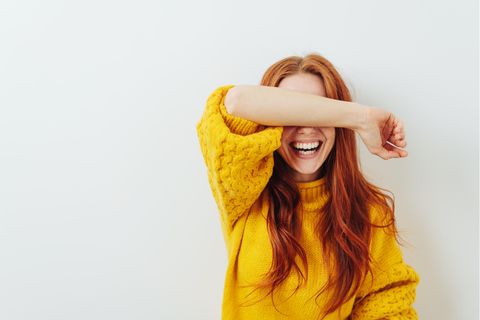 Frau mit roten Haaren und gelben Pulli hält sich den Arm vor die Augen