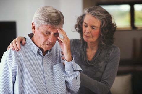 Ein Mann fasst sich an den Kopf, seine Frau stützt ihn an seinen Schultern
