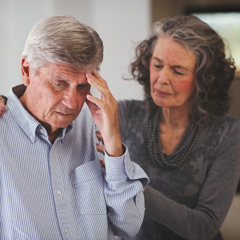 Ein Mann fasst sich an den Kopf, seine Frau stützt ihn an seinen Schultern