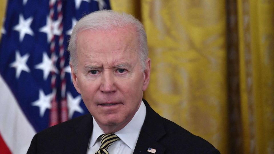Joe Biden Ein alter weißer Mann mit weißem Haar steht in Anzug und Krawatte vor einer US-Flagge und schaut böse