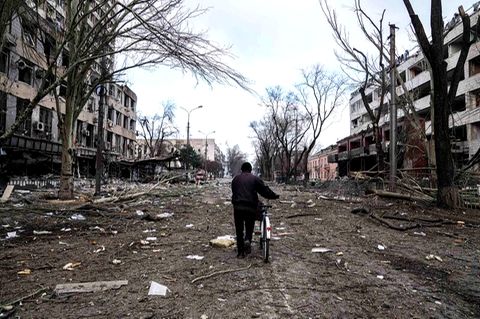 Ein Mann mit Fahrrad geht eine zerbombte Straße entlang