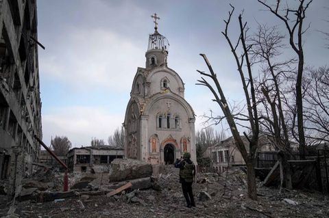 Eine Kirche steht in einem Trümmerfeld, davor steht ein Mann und nimmt ein Foto auf