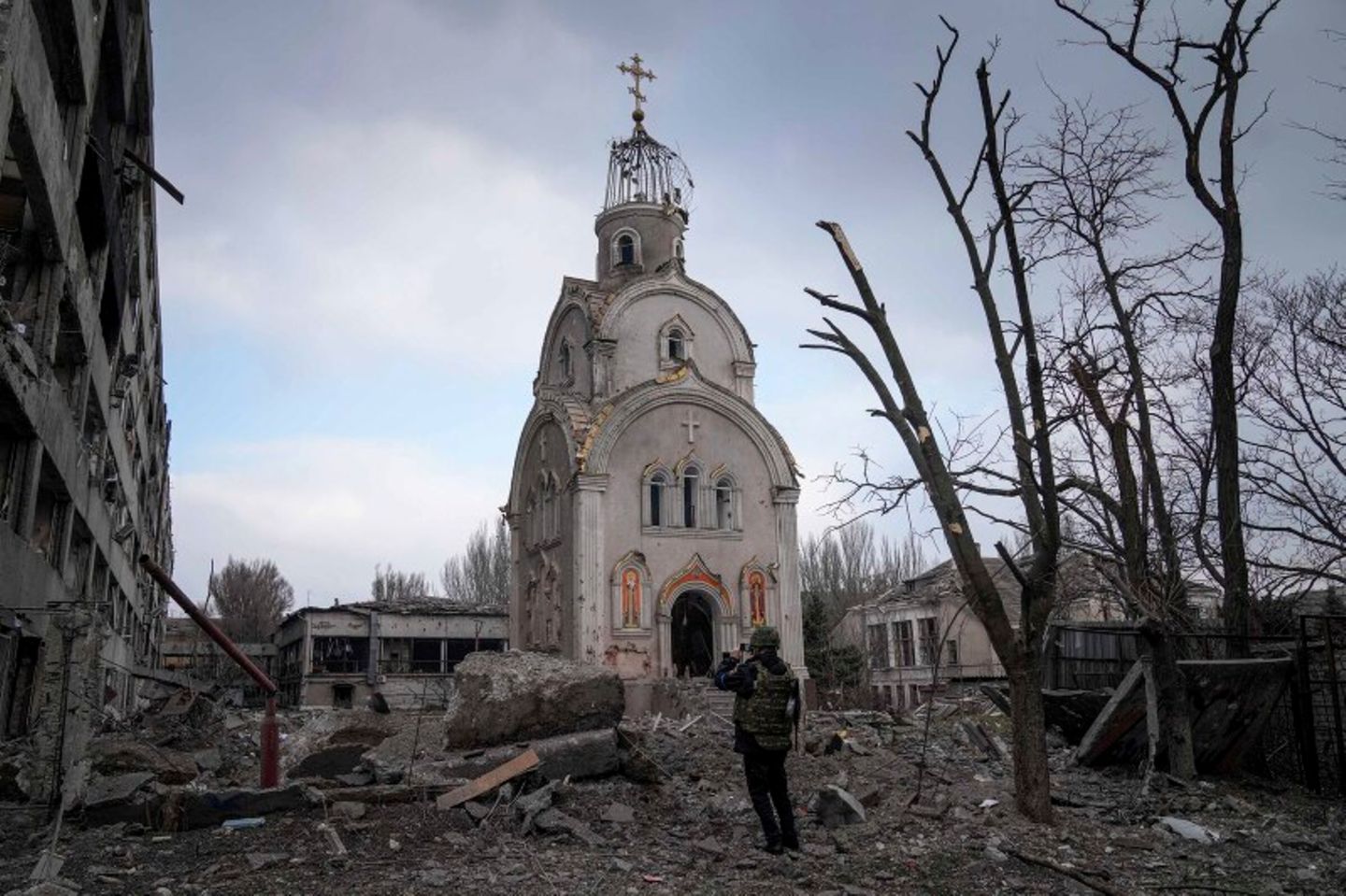 Eine Kirche steht in einem Trümmerfeld, davor steht ein Mann und nimmt ein Foto auf
