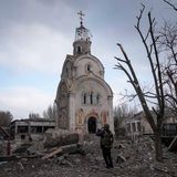 Eine Kirche steht in einem Trümmerfeld, davor steht ein Mann und nimmt ein Foto auf