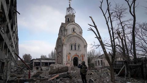Eine Kirche steht in einem Trümmerfeld, davor steht ein Mann und nimmt ein Foto auf