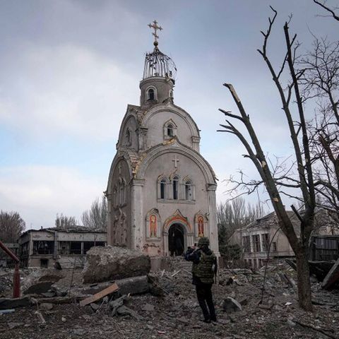 Eine Kirche steht in einem Trümmerfeld, davor steht ein Mann und nimmt ein Foto auf