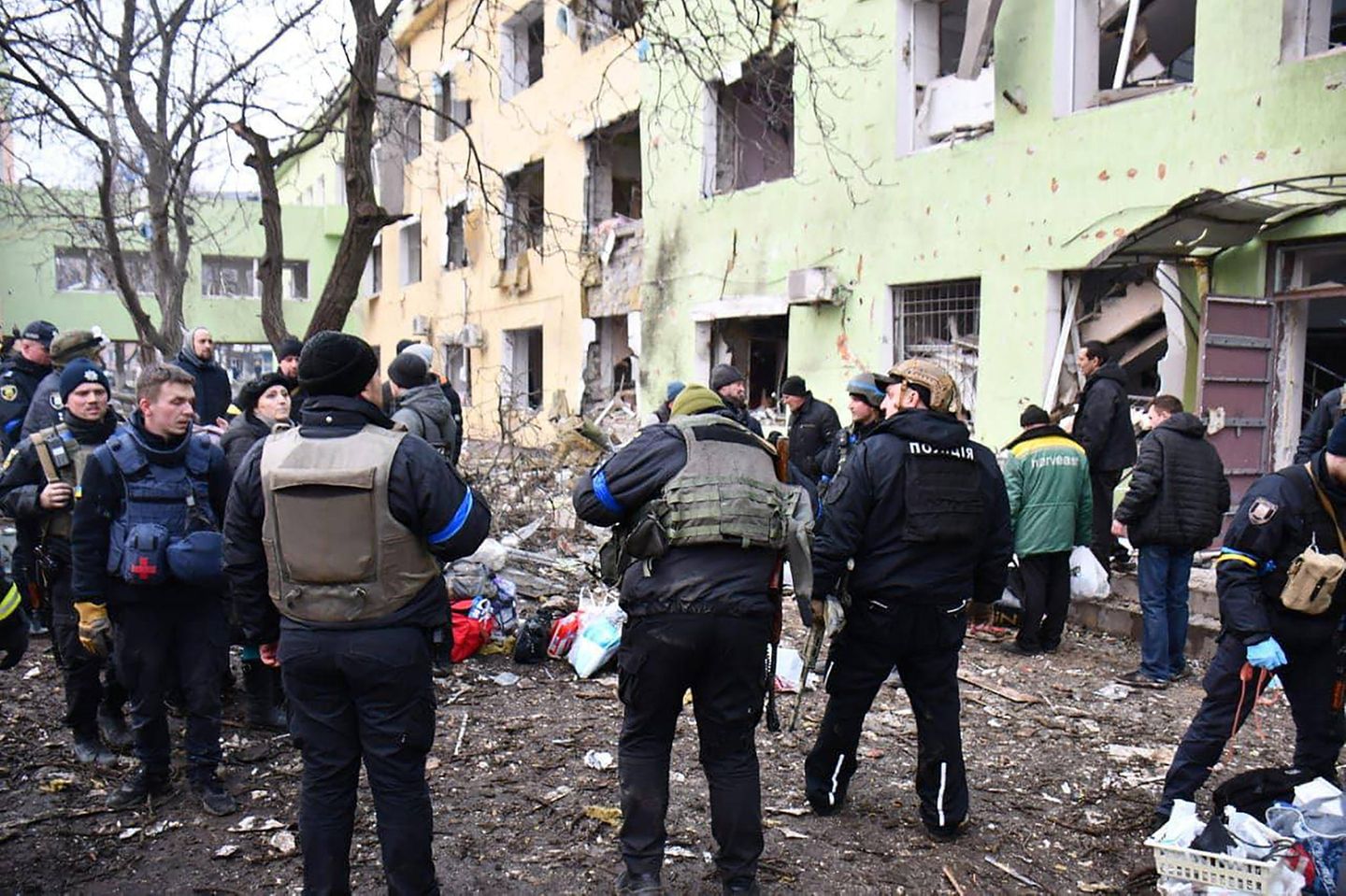 Vor einem beschädigten Mehrfamilienhaus steht eine Menschenmenge Vor einem beschädigten Mehrfamilienhaus steht eine Menschenmenge