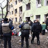 Vor einem beschädigten Mehrfamilienhaus steht eine Menschenmenge