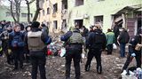 Vor einem beschädigten Mehrfamilienhaus steht eine Menschenmenge