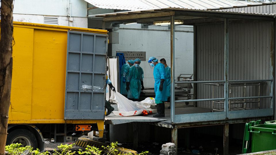 Krankenhausangestellte in Schutzanzügen verladen Leichen in Kühlwagen