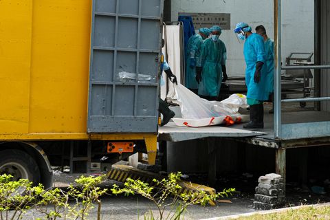Krankenhausangestellte in Schutzanzügen verladen Leichen in Kühlwagen