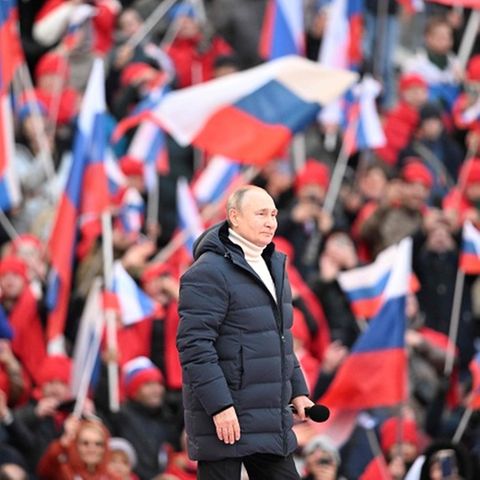 Wladimir Putin inmitten von Menschen mit russischen Flaggen, er trägt eine gefütterte jacke