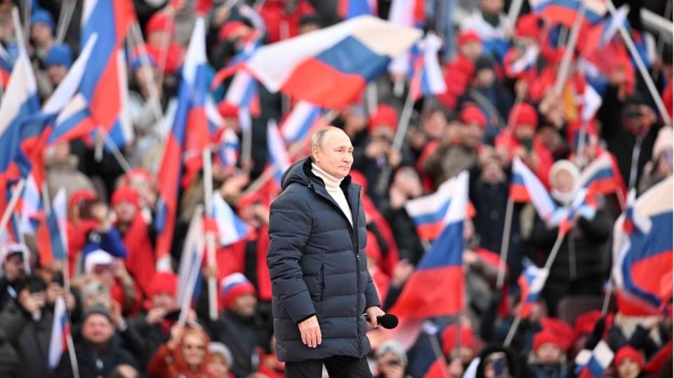 Wladimir Putin inmitten von Menschen mit russischen Flaggen, er trägt eine gefütterte jacke