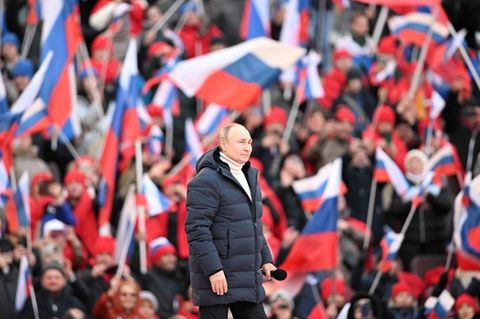 Wladimir Putin inmitten von Menschen mit russischen Flaggen, er trägt eine gefütterte jacke