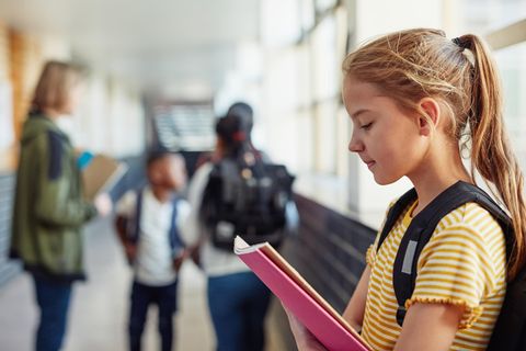 Mädchen steht abseits von anderen Kindern auf dem Schulflur