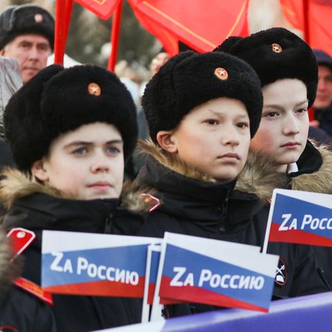 Schüler stehen in einem Park in Russland mit "Für Russland"-Fähnchen