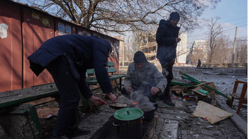 Männer kochen eine Mahlzeit in einer Straße in Mariupol, Ukraine Männer kochen eine Mahlzeit in einer Straße in Mariupol, Ukraine