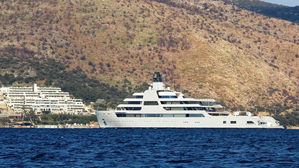Solaris Yacht Abramowitsch Eine riesige weiße Motoryacht liegt vor einer karg bewachsenen Küste in der Sonne