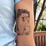 Eine nackte Mutter mit Blumen im Haar, die ihr schlafendes Kind eng umschlungen hält ist auf einen Arm tätowiert