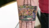 Ein Gemälde auf einer Staffelei zeigt Menschen im Park. Es steht auf einer Staffelei und ist ein Tattoo auf einem Arm.