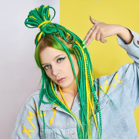 Junge Frau mit bunten Dreadlocks hält sich Hand an den Kopf