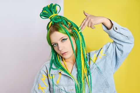 Junge Frau mit bunten Dreadlocks hält sich Hand an den Kopf