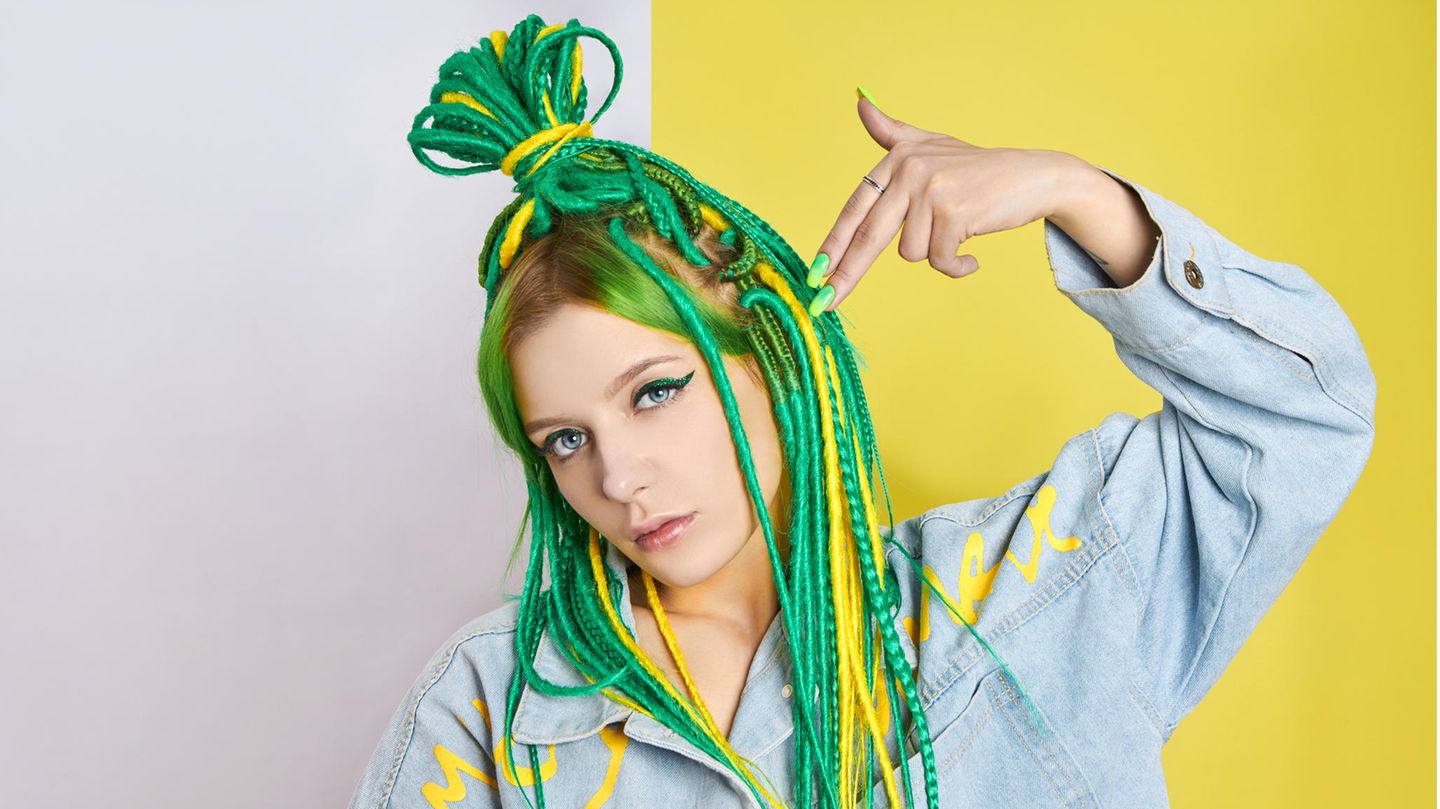 Junge Frau mit bunten Dreadlocks hält sich Hand an den Kopf