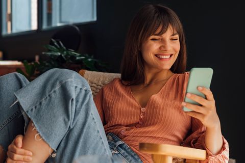 Eine Frau sitzt auf einem Sessel und hält ein Smartphone in der Hand