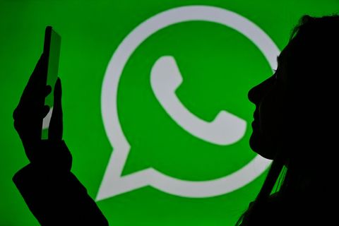 Eine Frau schaut auf ein Smartphone, dahinter das Whatsapp-Logo