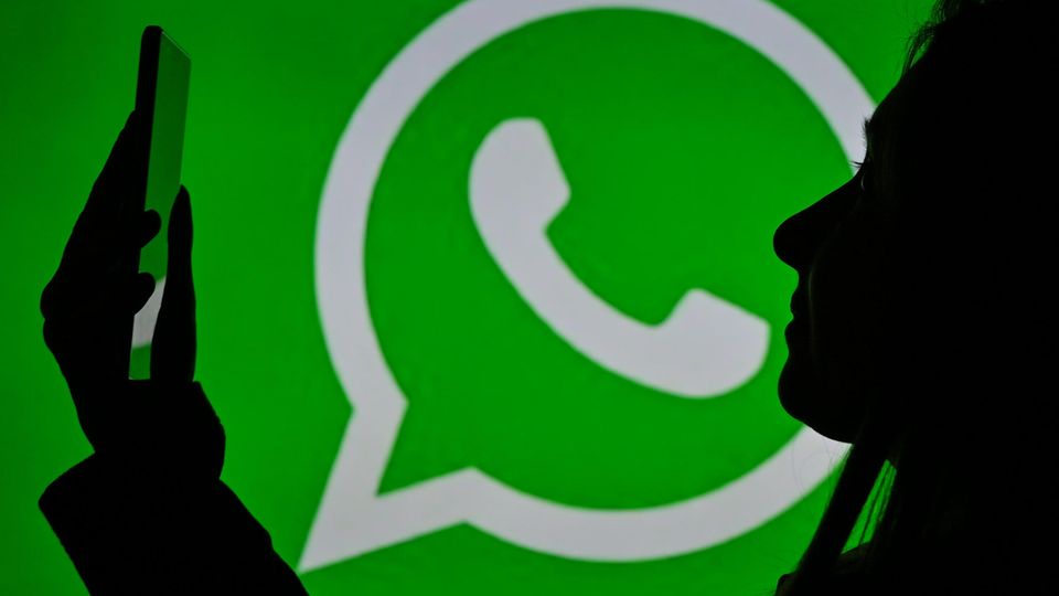 Eine Frau schaut auf ein Smartphone, dahinter das Whatsapp-Logo